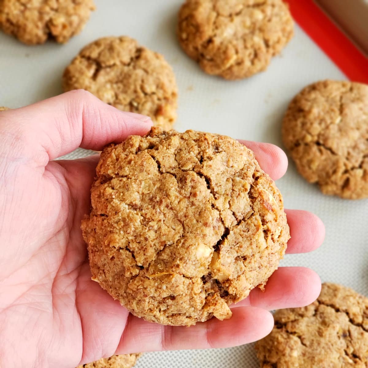 Hand holding a large Banana Almond Butter Breakfast Cookie with other cookies in the background