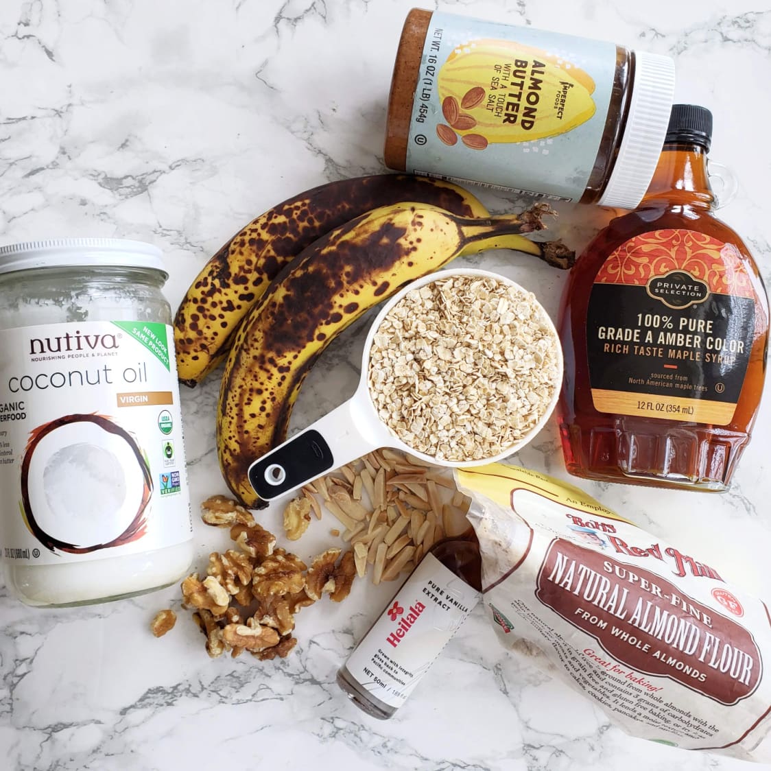 Ingredients for Roasted Banana Almond Butter Breakfast Cookies gathered on a white marble counter