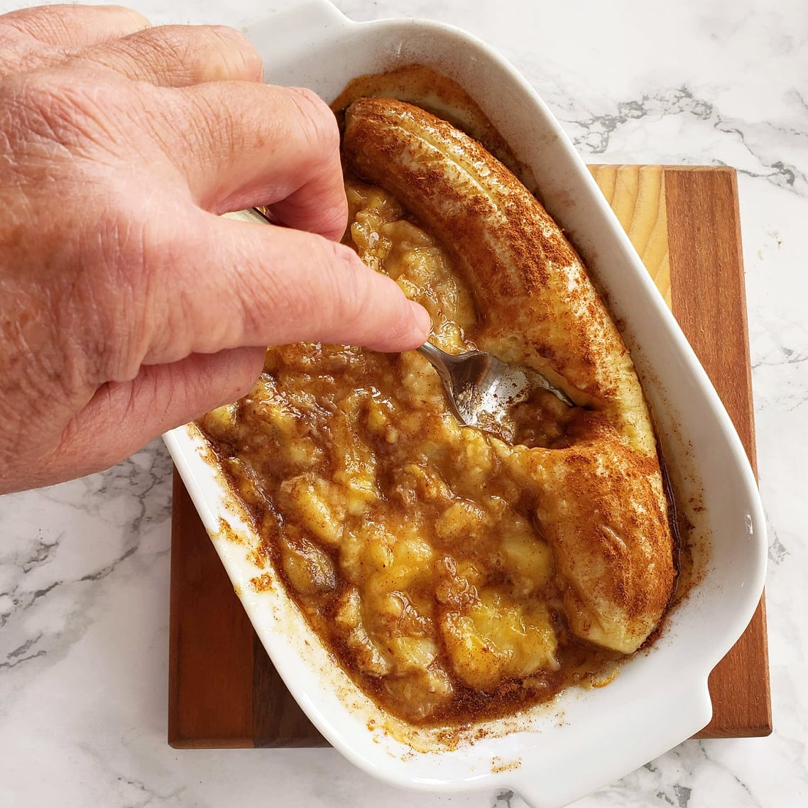 Mash bananas with a fork in a white baking dish on a wooden board