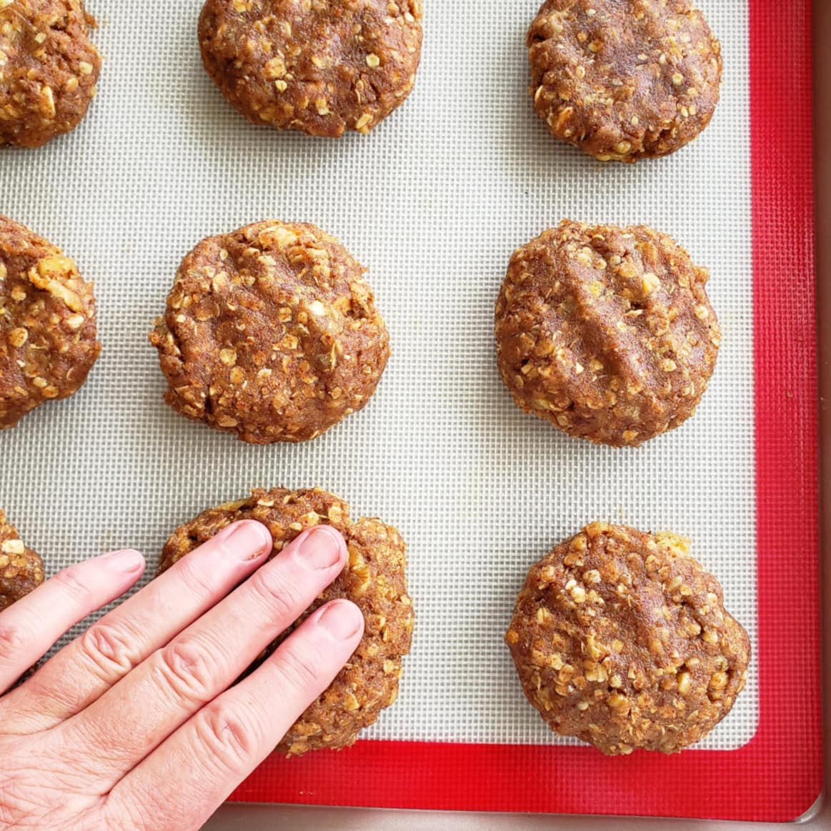 9 cookies on a baking sheet being pressed by a hand