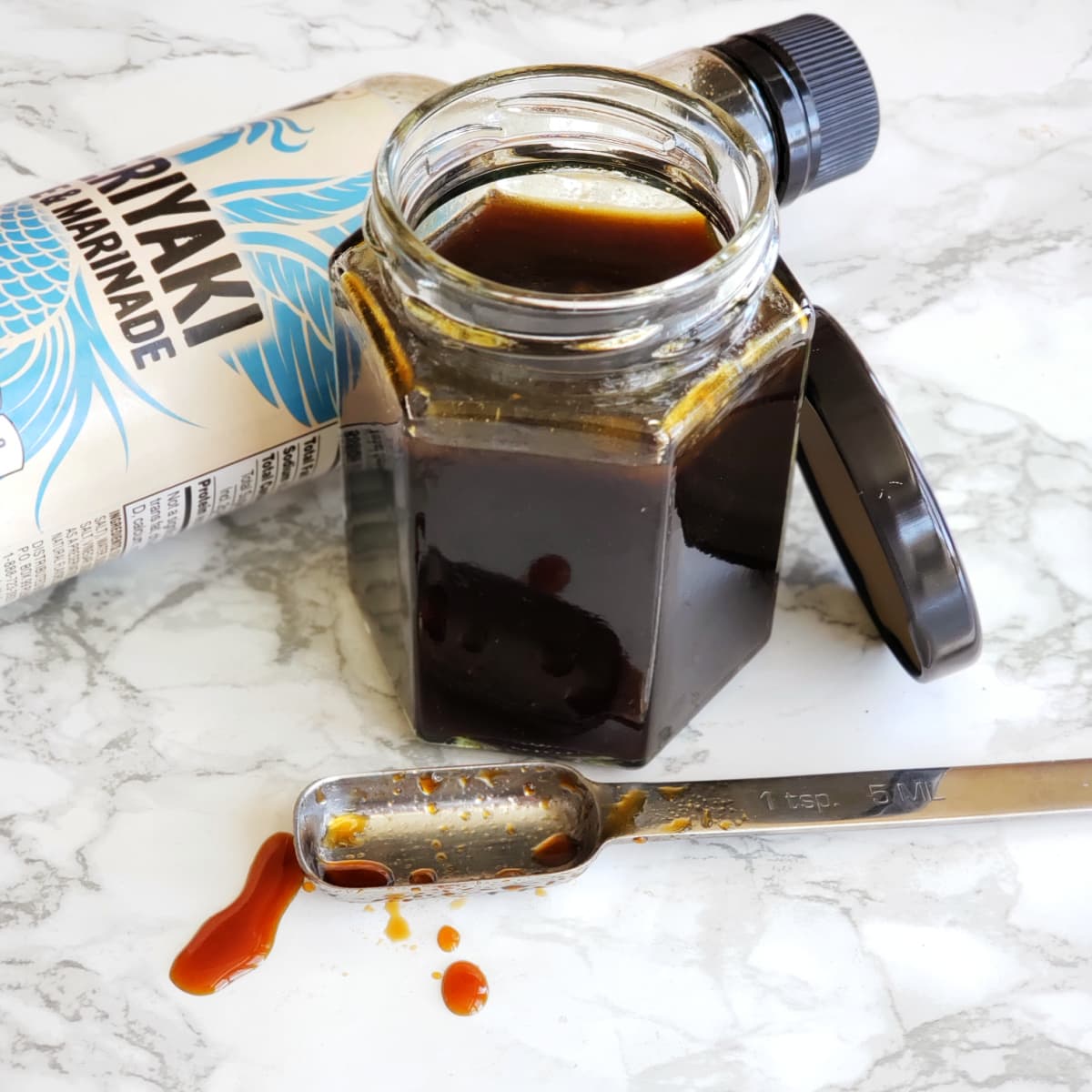 Homemade Teriyaki Sauce in a six-sided glass jar on a white marble counter on ShockinglyDelicious.com