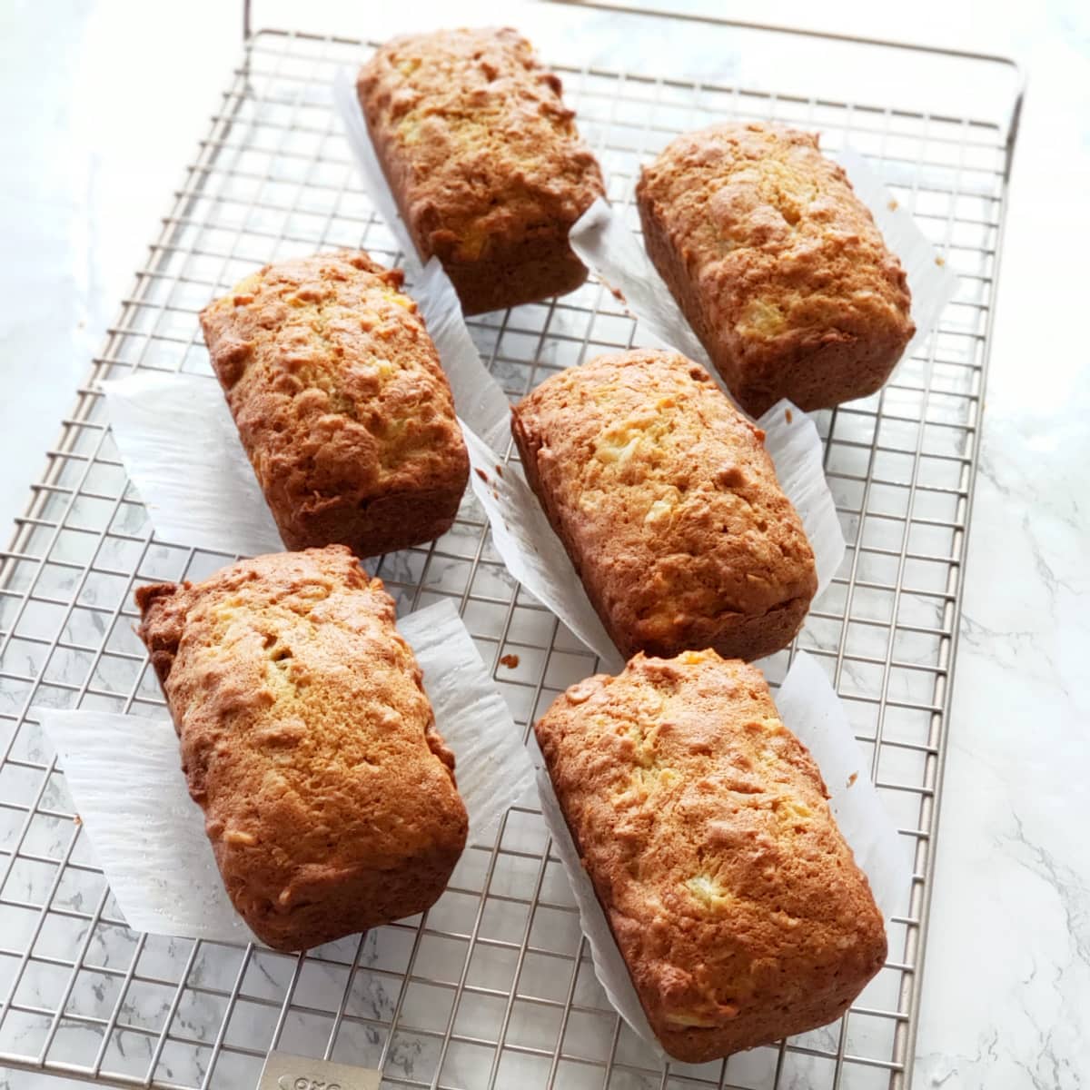 6 Pineapple Coconut Quick Bread baked loaves cooling on a wire rack on a white marble counter