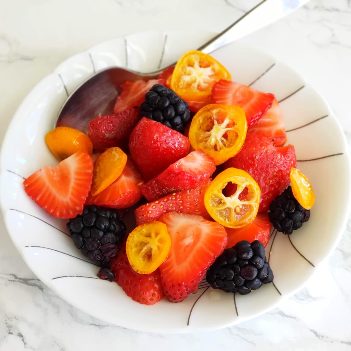 White bowl of strawberries and blackberries with No-Cook Candied Kumquats on ShockinglyDelicious.com