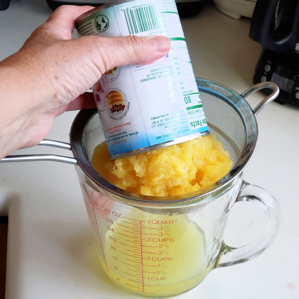Pineapple draining in a mesh drainer into a glass measuring cup on a white counter