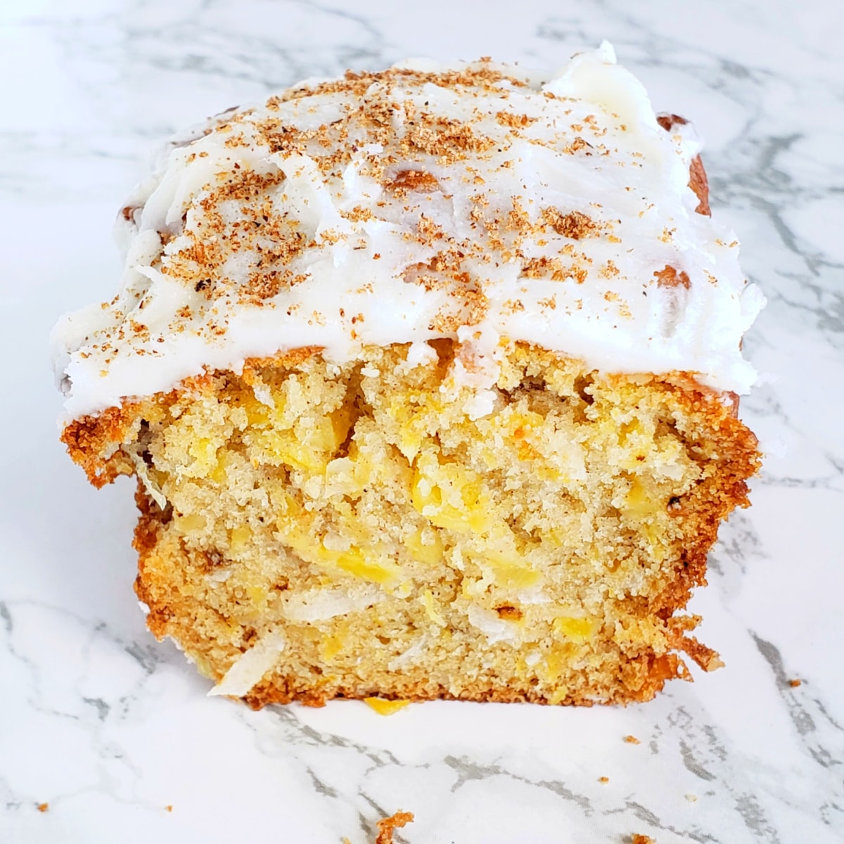 Easy Pineapple Coconut Quick Bread small loaf cut in half, displayed on a white marble counter, on ShockinglyDelicious.com