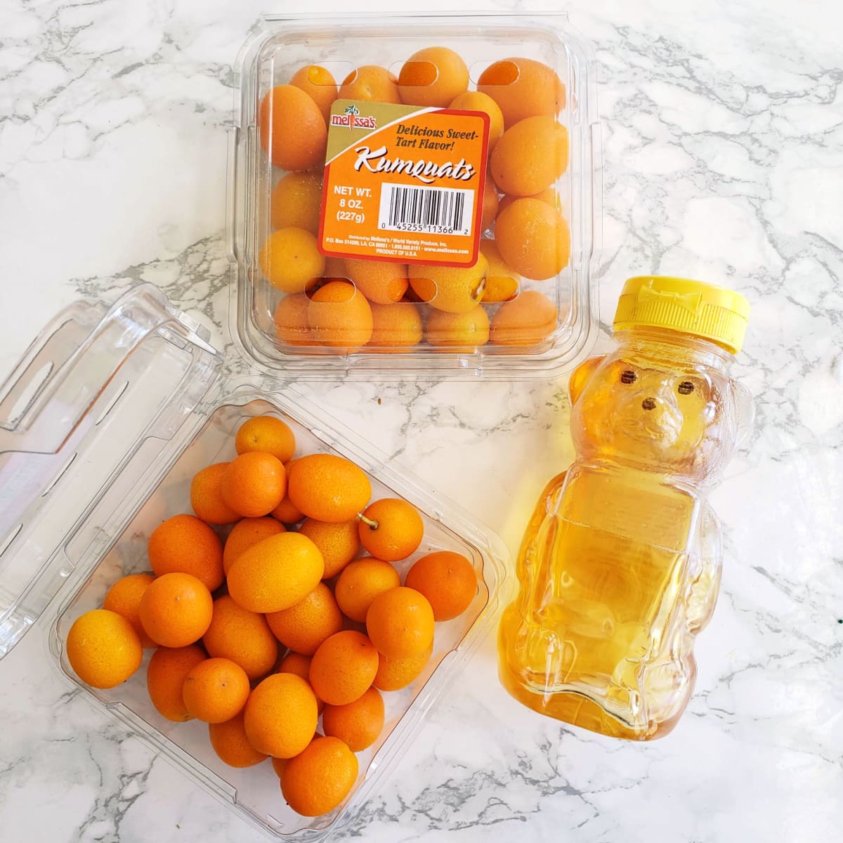 Kumquats and honey on a white marble counter