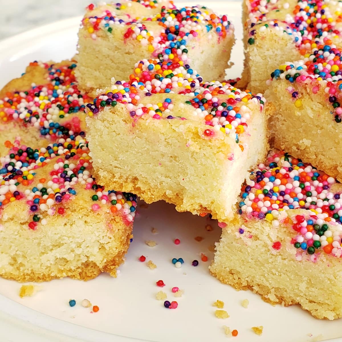 Lemon Shortbread squares with sprinkles on top piled on a white plate 