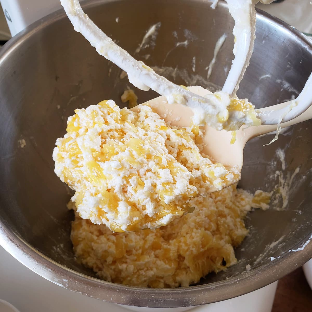 Curdled mixture with pineapple, on a white spoon in a silver mixer bowl
