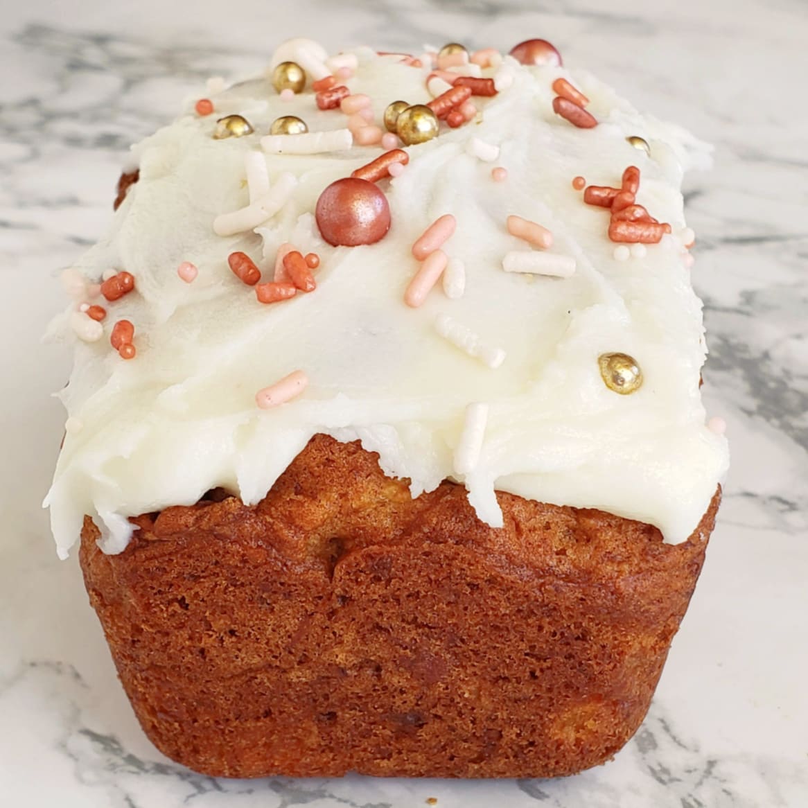 Simple Pineapple Coconut Quick Bread with frosting and sprinkles on a white marble counter