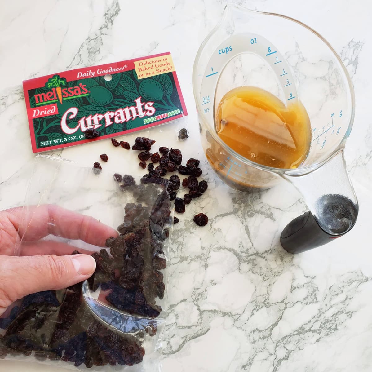 Currants will soak in tangerine juice in a measuring cup on a white marble counter 