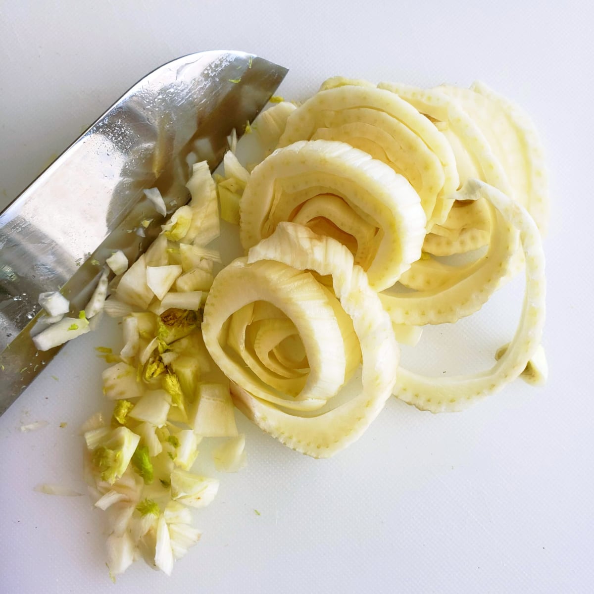 Cut fennel into rounds with a knife on a white cutting board