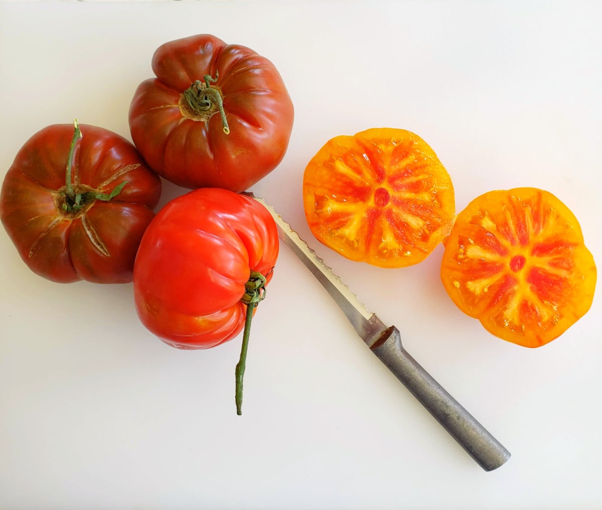 Heirloom tomatoes on a white cutting board with a knife