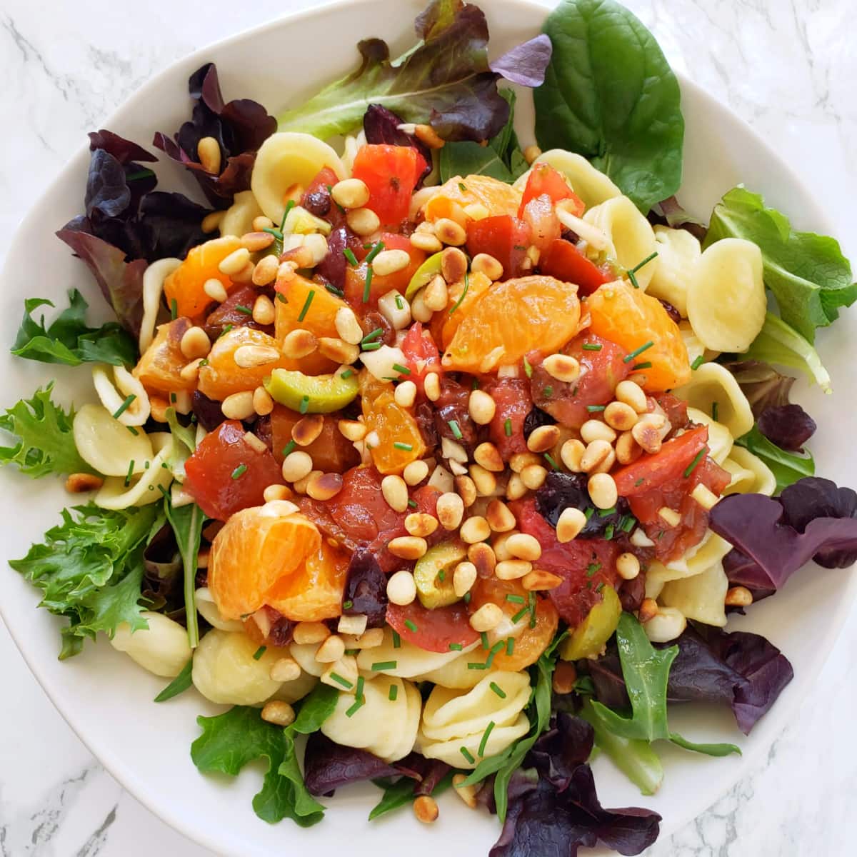 Pasta with Tomatoes and Tangerines vegan meal in a shallow white bowl on a marble counter