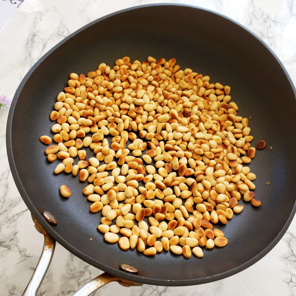Toasted pine nuts in a grey skillet