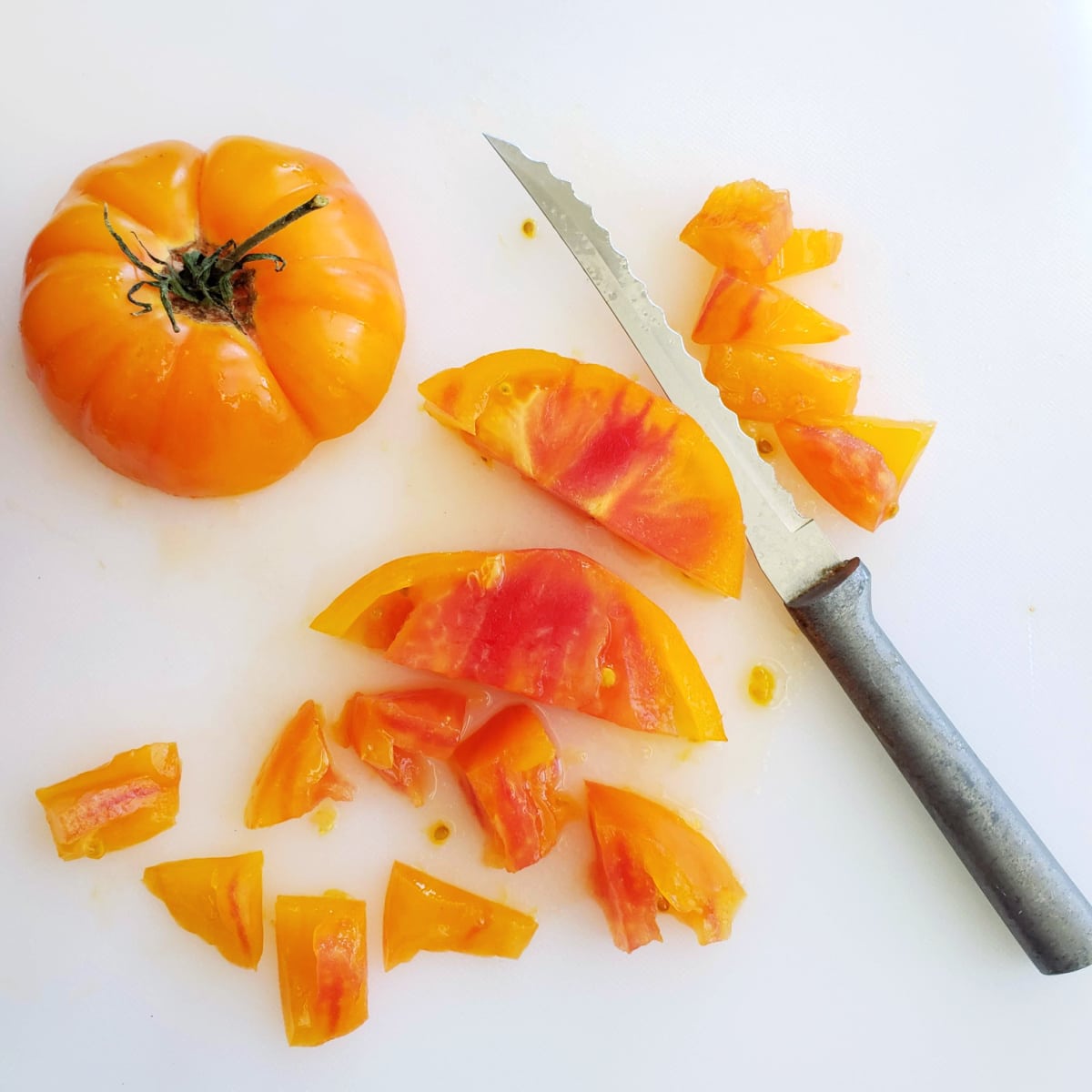 Yellow heirloom tomato on a white cutting board with a knife