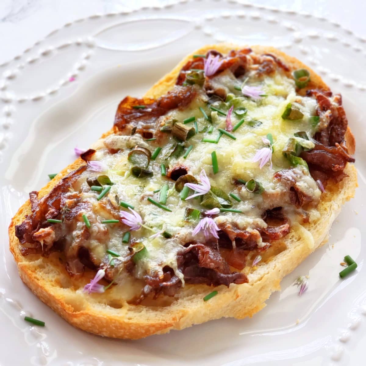 French Onion Open Faced Sandwich on a white textured plate with purple chive flowers decorating the top on ShockinglyDelicious.com