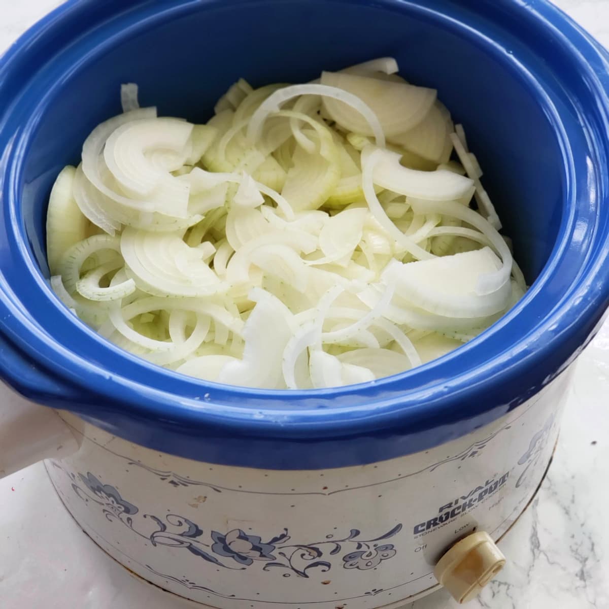 Onions in the blue crock of a slow cooker on ShockinglyDelicious.com