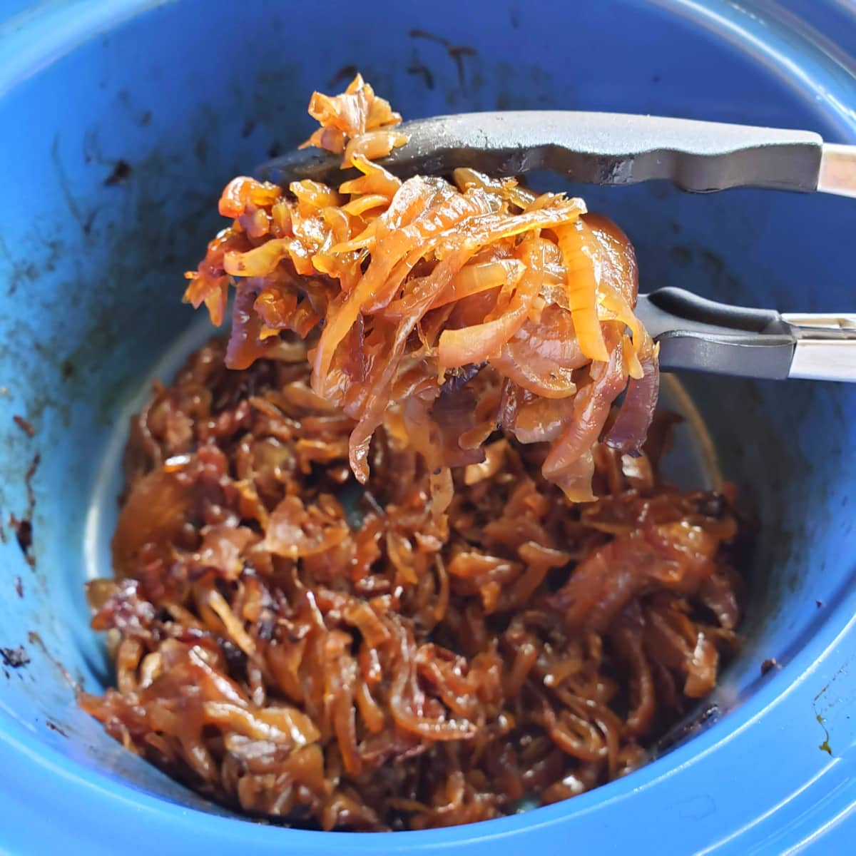 Tongs holding caramelized onions from a blue crock on ShockinglyDelicious.com