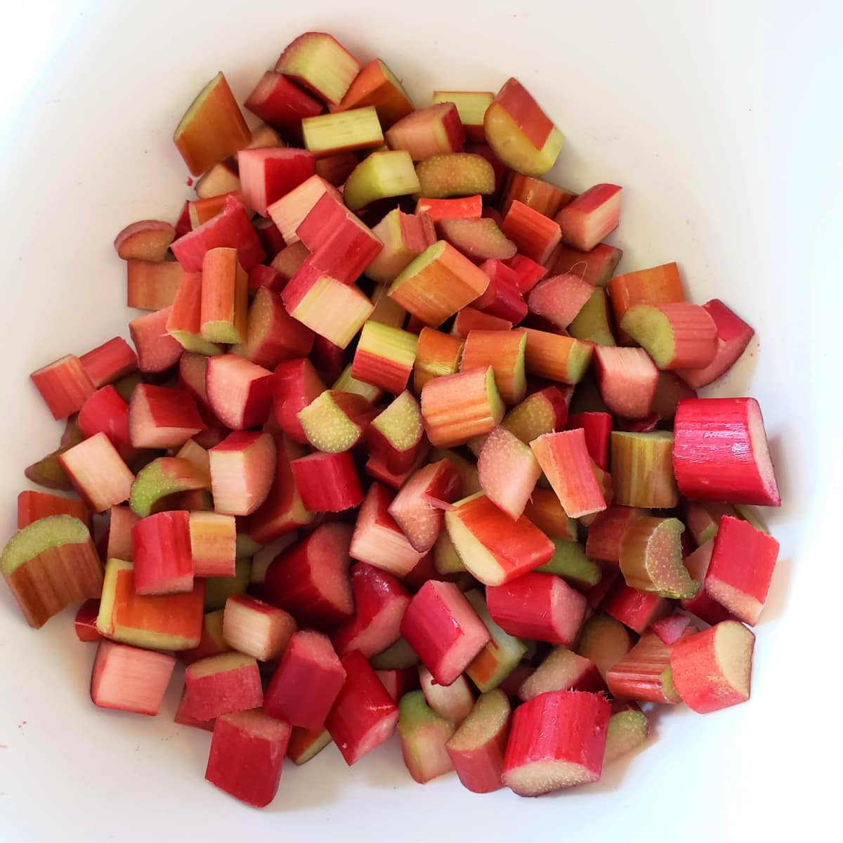 Bright red and green chopped rhubarb in a white mixing bowl on ShockinglyDelicious.com