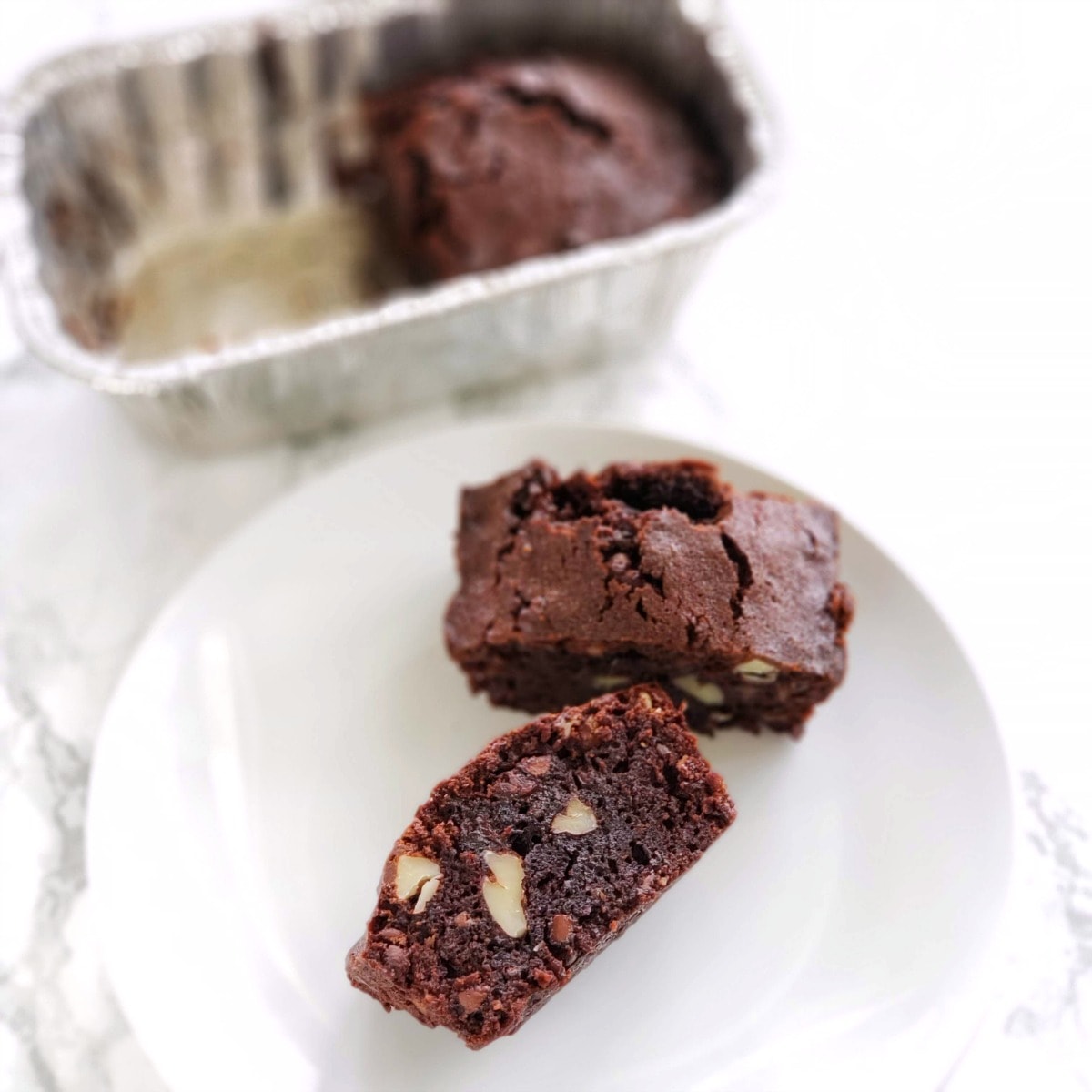 Small Batch Emergency Brownies 2 brownies on a white plate with a mini loaf pan behind with additional brownie in it