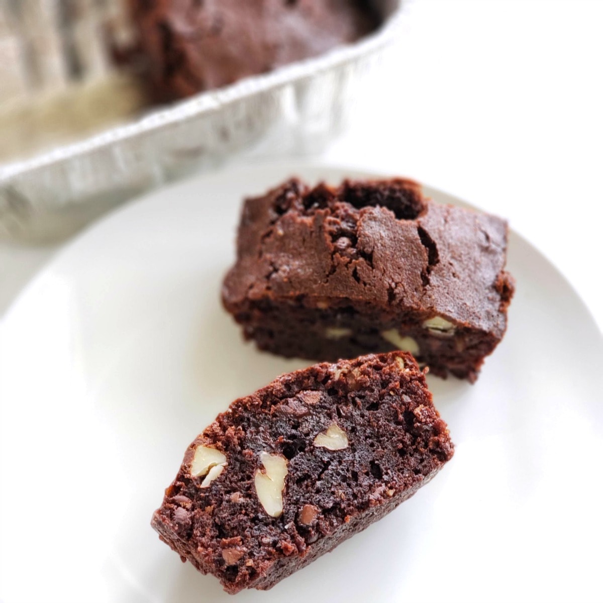 2 Emergency Brownies on a white plate with the foil pan of brownies in the background