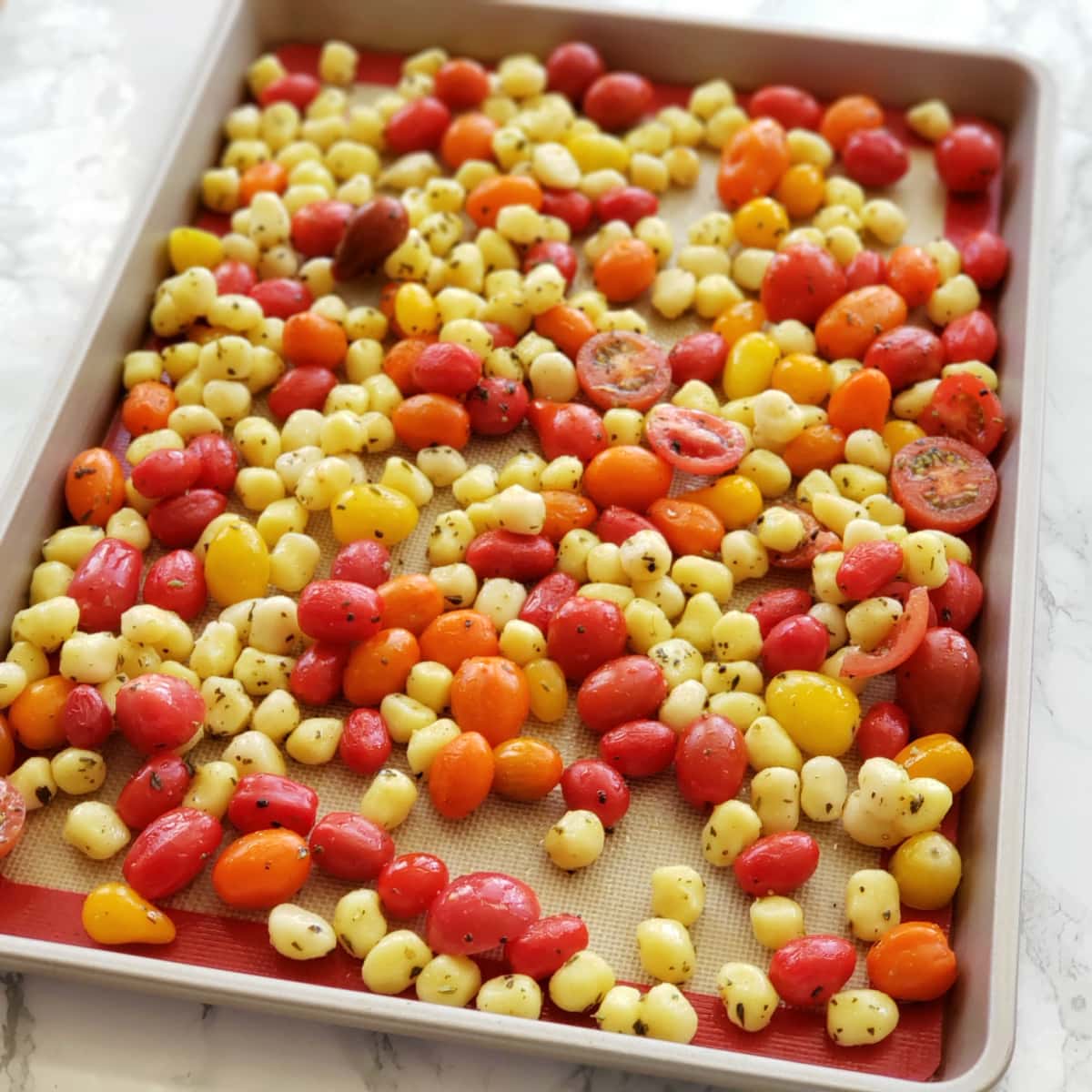 Gnocchi and tomatoes on a gold colored sheet pan on a white marble counter on ShockinglyDelicious.com