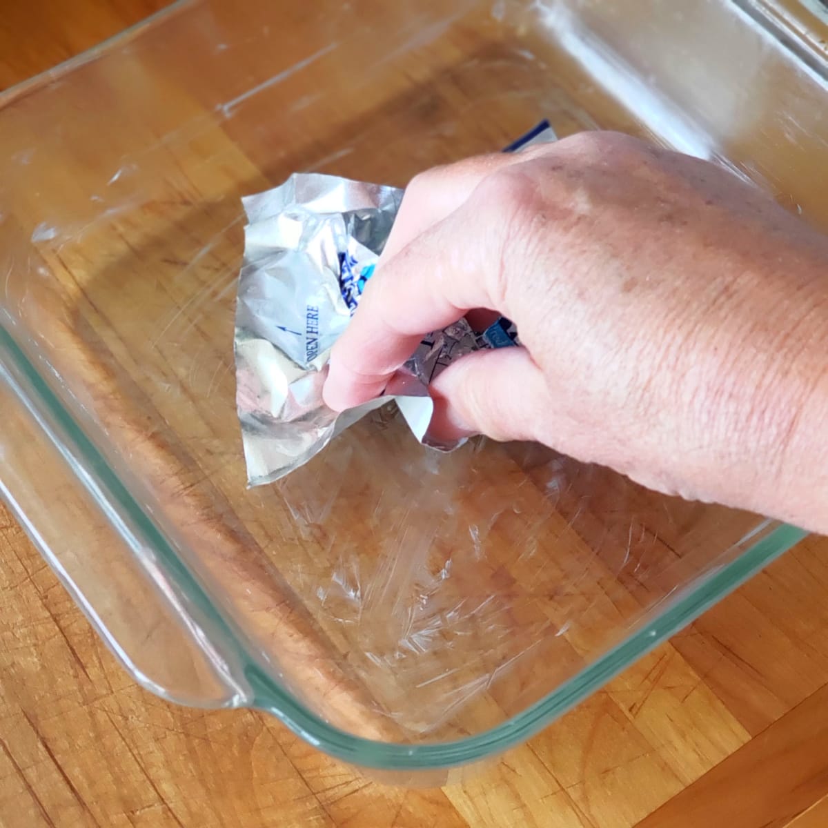 A hand holding the butter wrapper greases the glass baking dish on ShockinglyDelicious.com