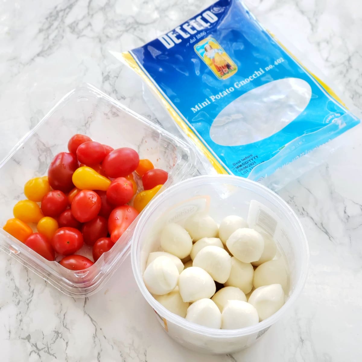 Ingredients for Sheet Pan Gnocchi with Cherry Tomatoes, Mozzarella and Arugula on a white marble counter on ShockinglyDelicious.com