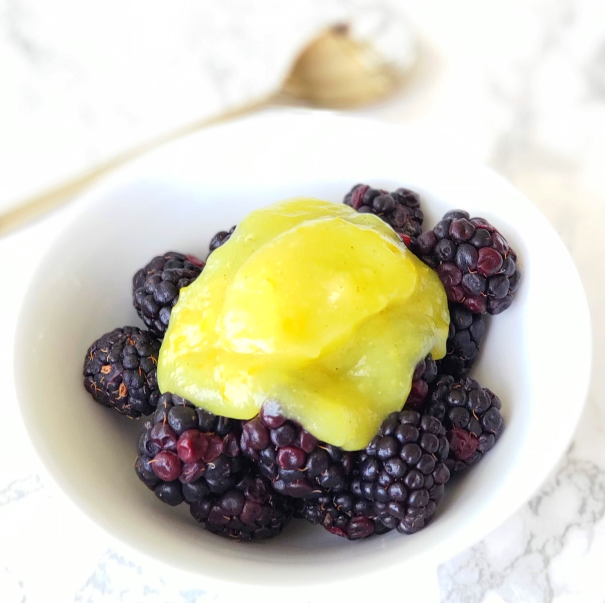 Lemon filling is dolloped onto a white bowl of blackberries 