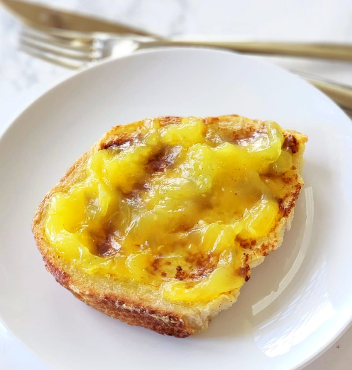 Lemon Filling spread thickly on Toast on a white plate with silverware behind it