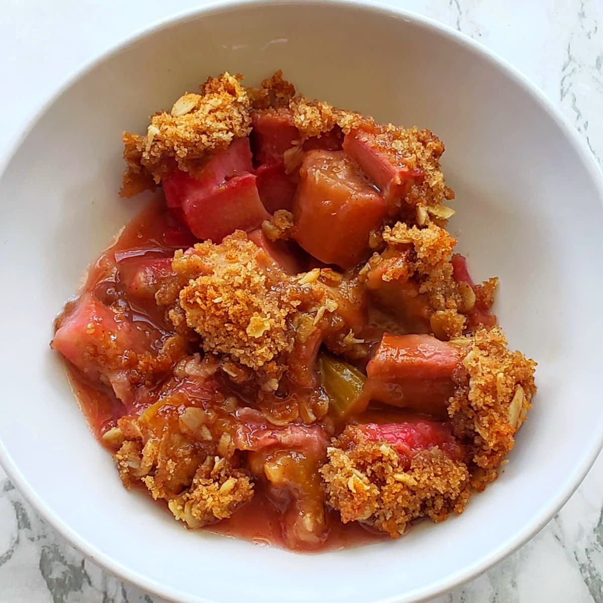 Rhubarb Crumble in a white bowl with visible rhubarb chunks topped by streusel