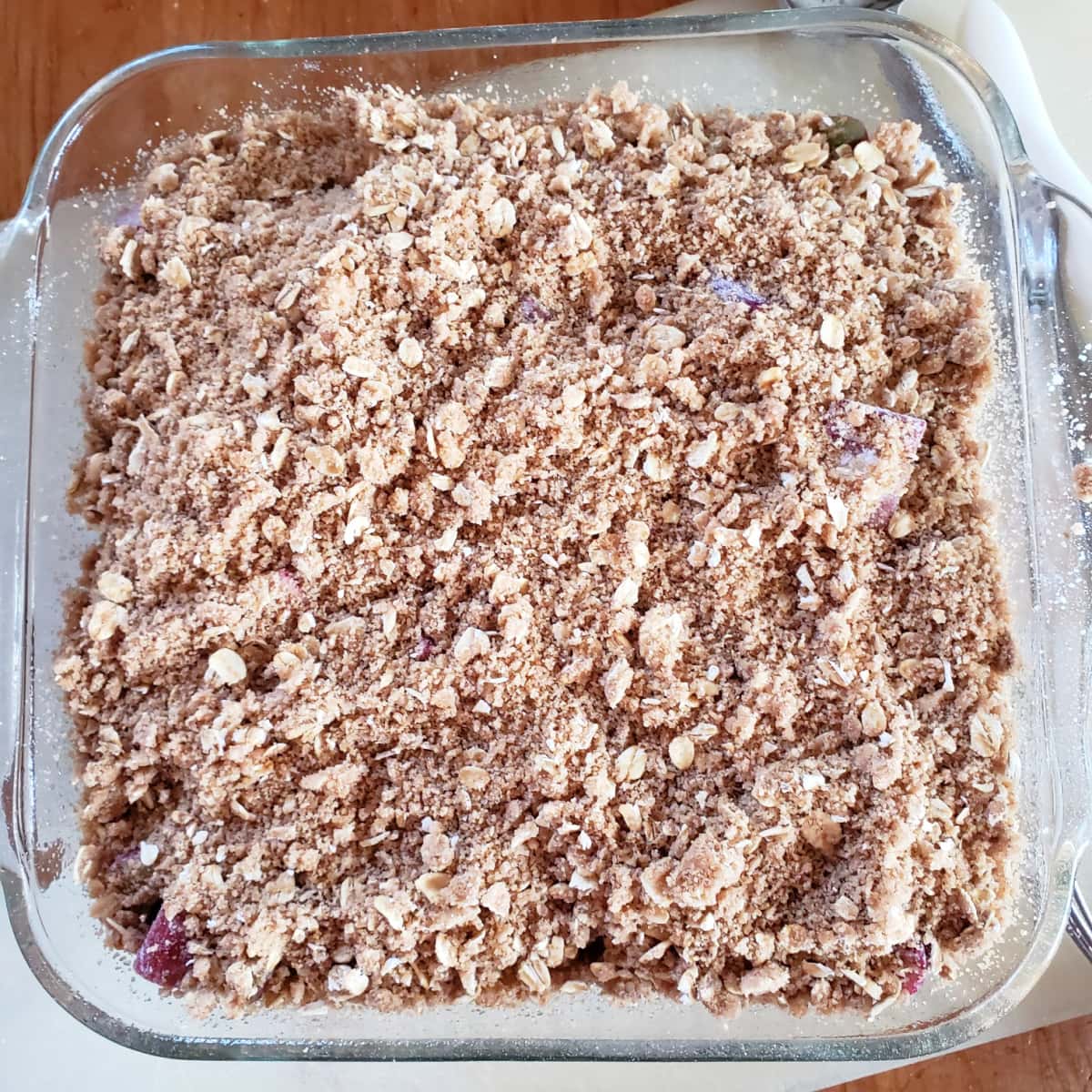 Square glass baking dish with rhubarb with streusel on top on a white cutting board