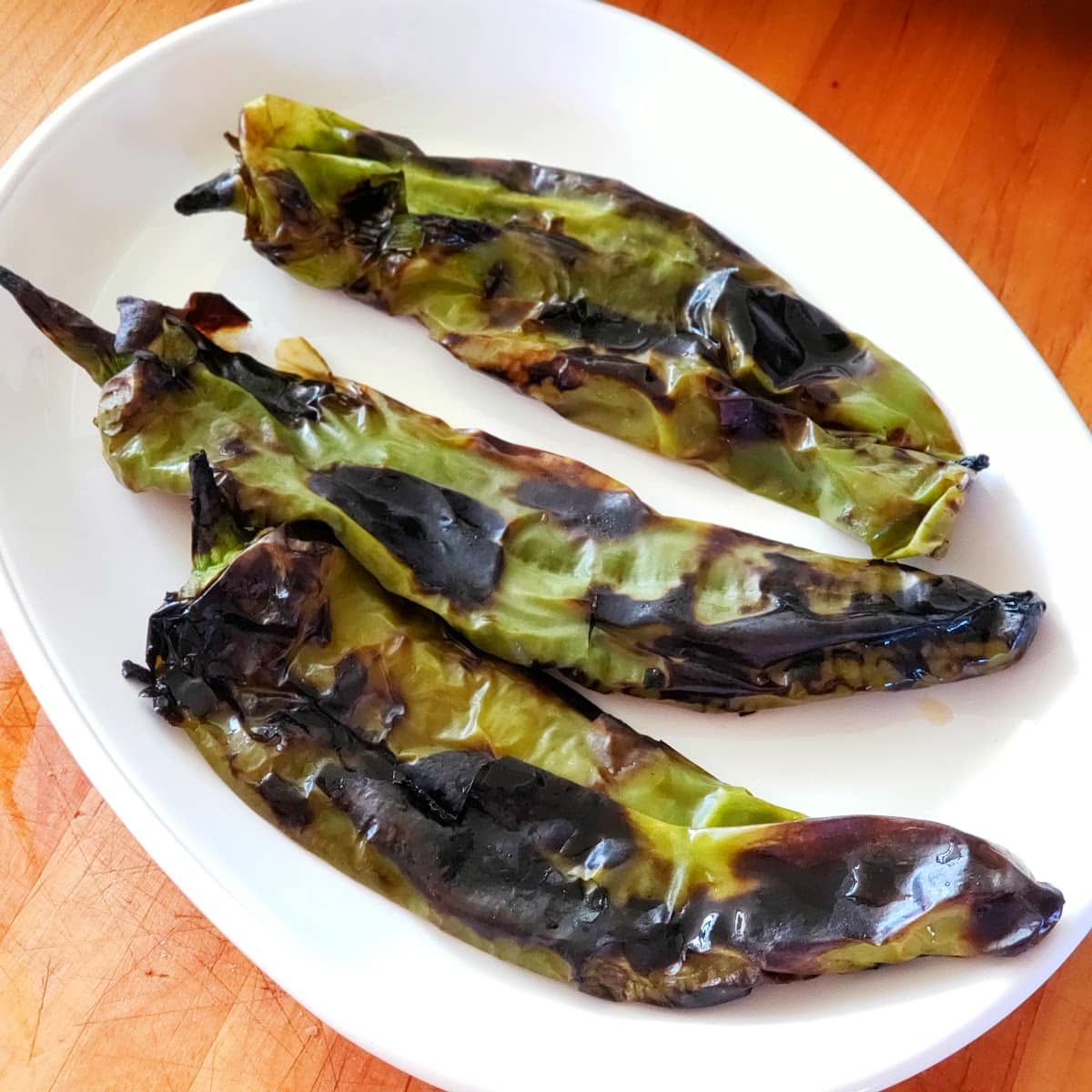 3 roasted Hatch chiles on a white plate on ShockinglyDelicious.com