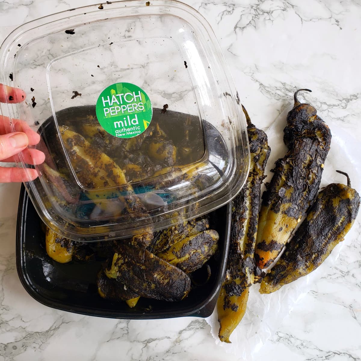 Roasted Hatch chile peppers in a black clamshell package on a white marble counter on ShockinglyDelicious.com