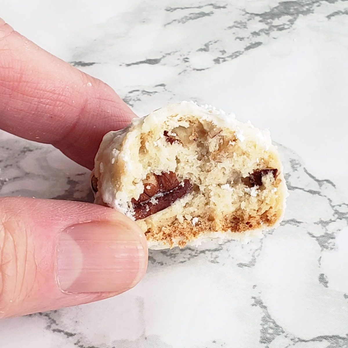 Thumb and finger holding a half-bitten Mexican Wedding Cookie showing the inside