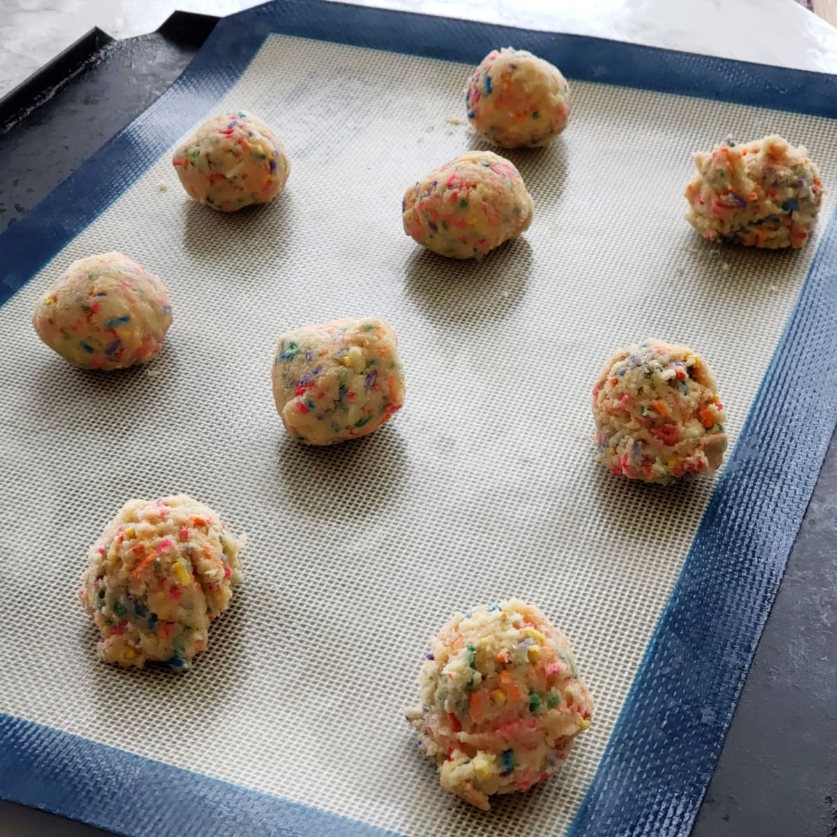 9 balls of cookie dough on a silicone lined baking sheet ready to bake
