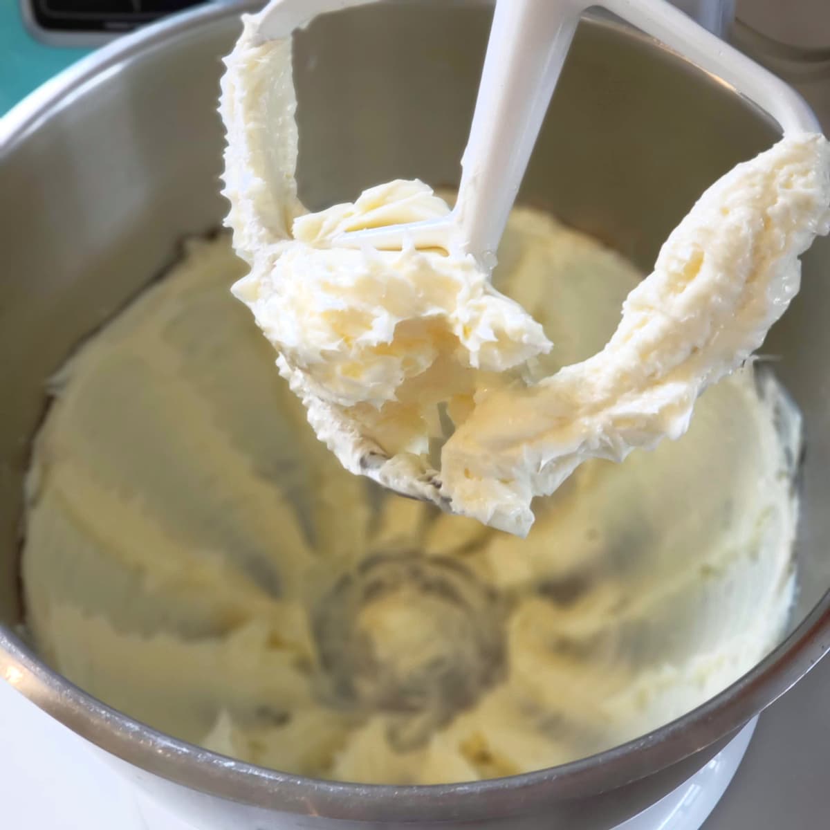 Creamed butter clumped on the beater of a stand mixer, with a silver bowl underneath