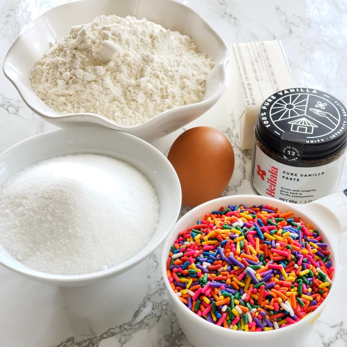 Ingredients for Confetti Sprinkle Cookies on a white marble countertop on ShockinglyDelicious.com