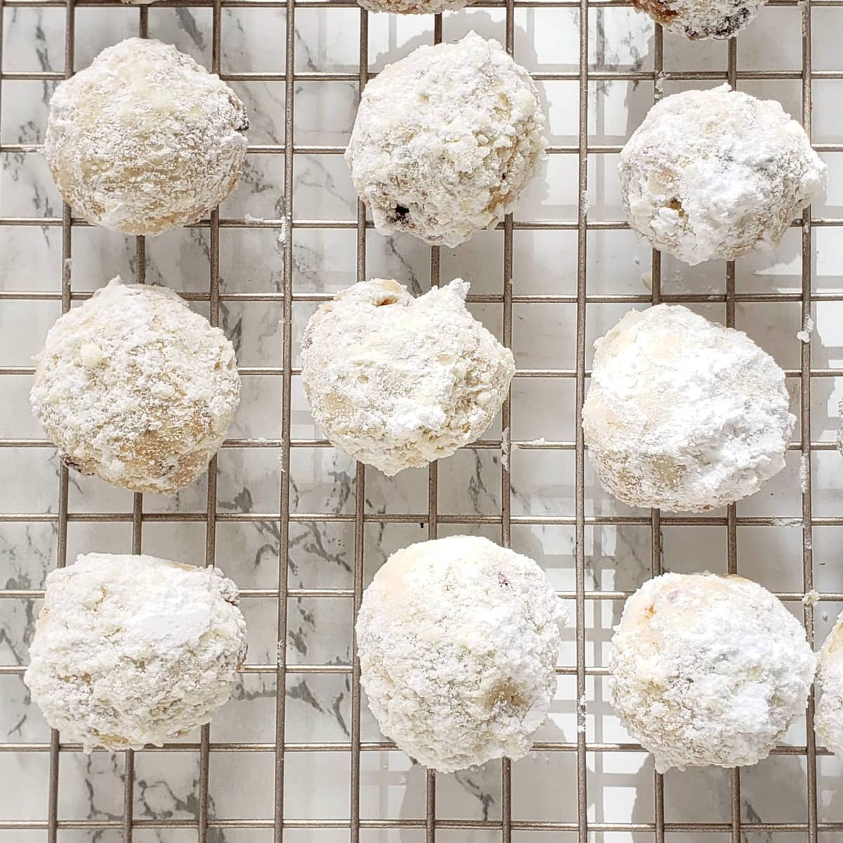 9 white sugar-dusted round cookies on a cooling rack on a white marble counter