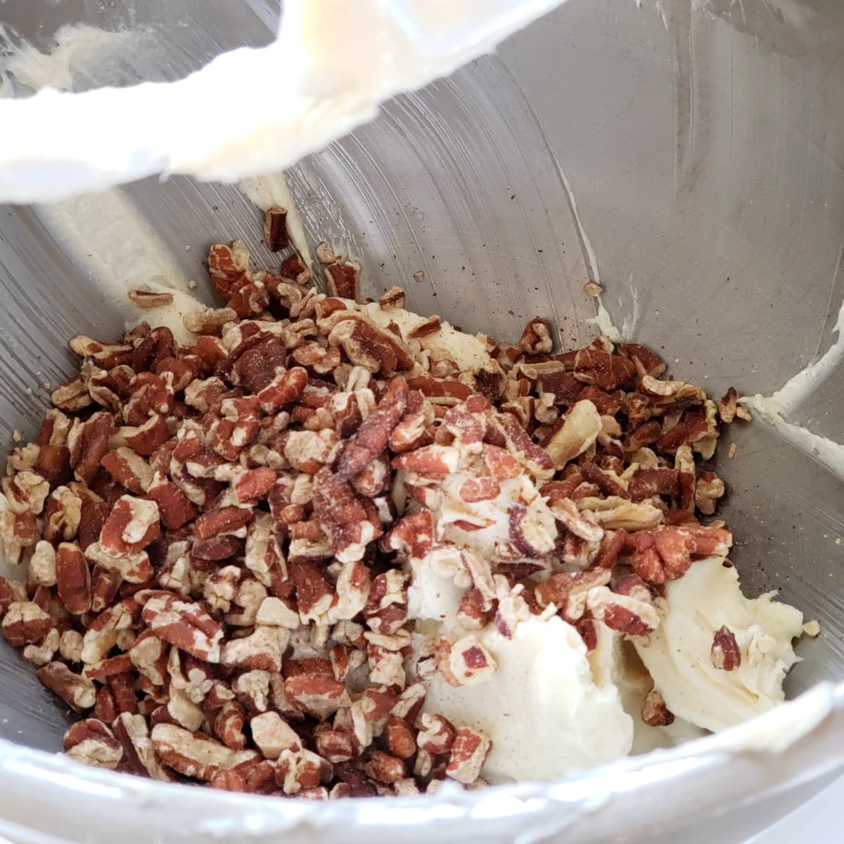 A pile of chopped pecans on top of beige cookie dough in the silver mixing bowl 