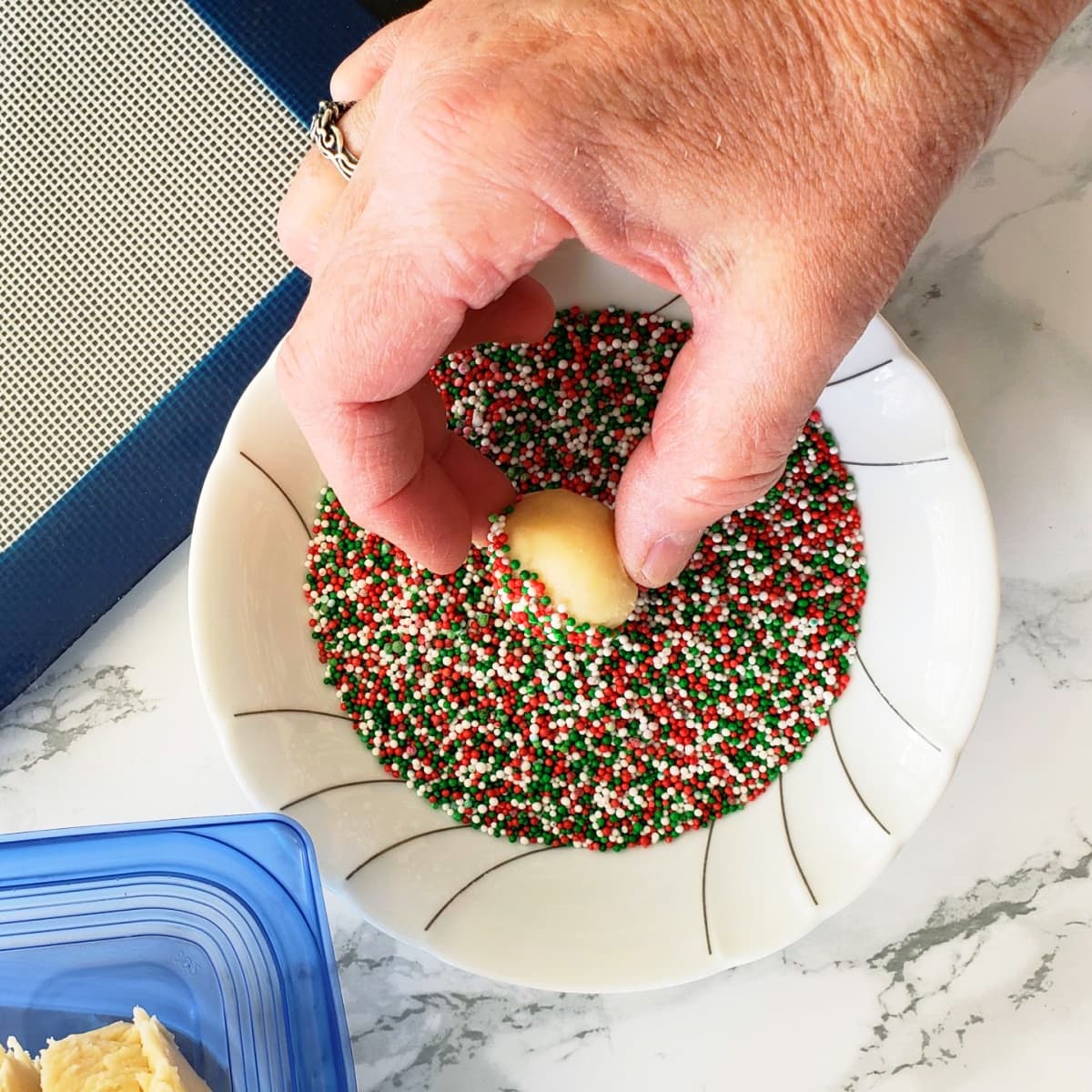 A hand rolls cookie ball into nonpareils in a white bowl
