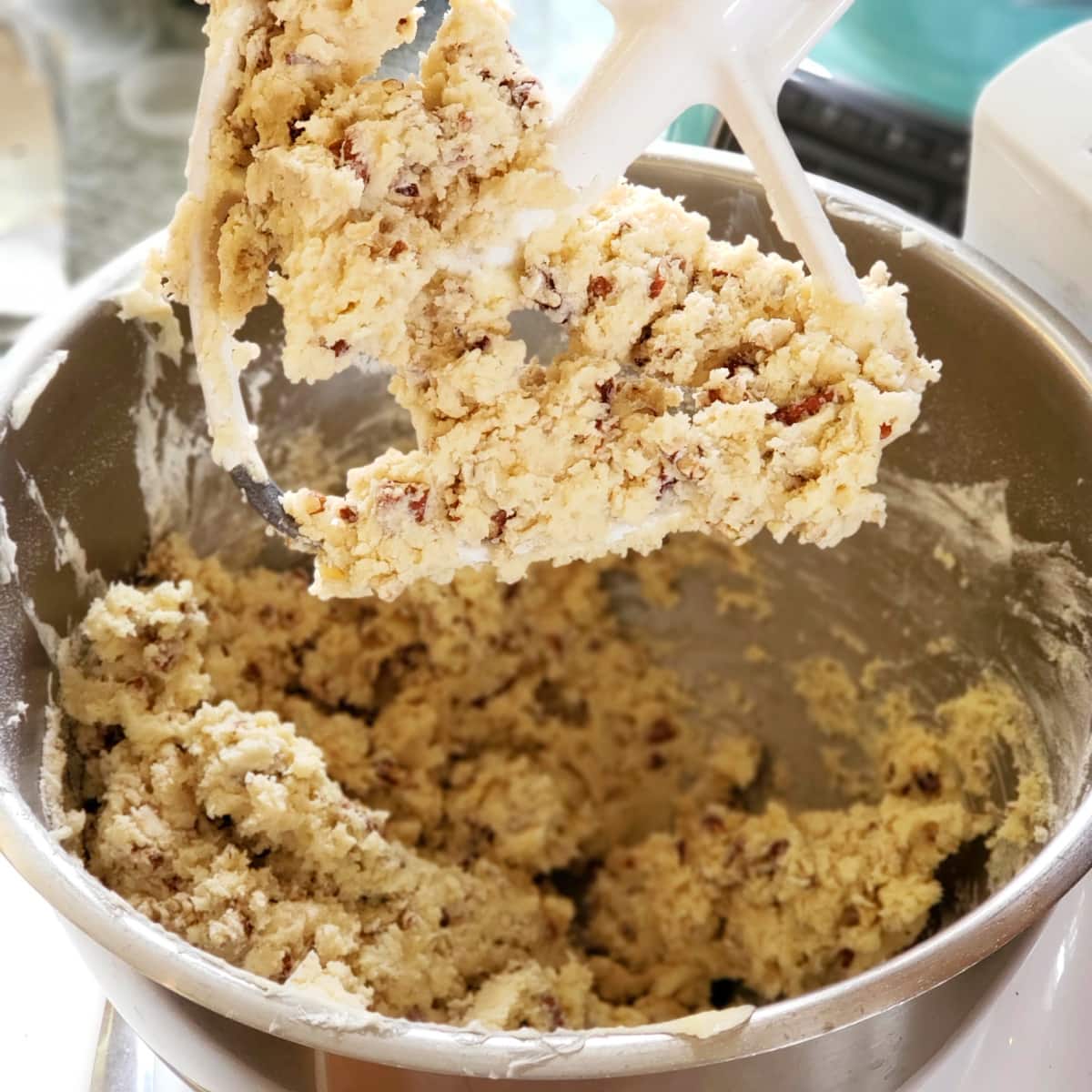 Thick pecan dough for Mexican Wedding Cookies clings to the white beater of a stand mixer