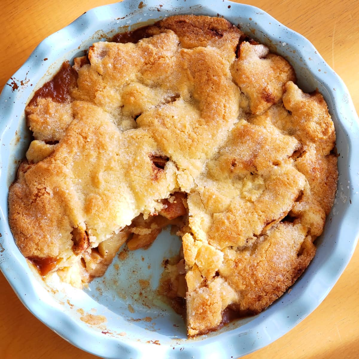 One piece cut out of a Swedish Apple Pie in a light blue pie dish sitting on a wood table