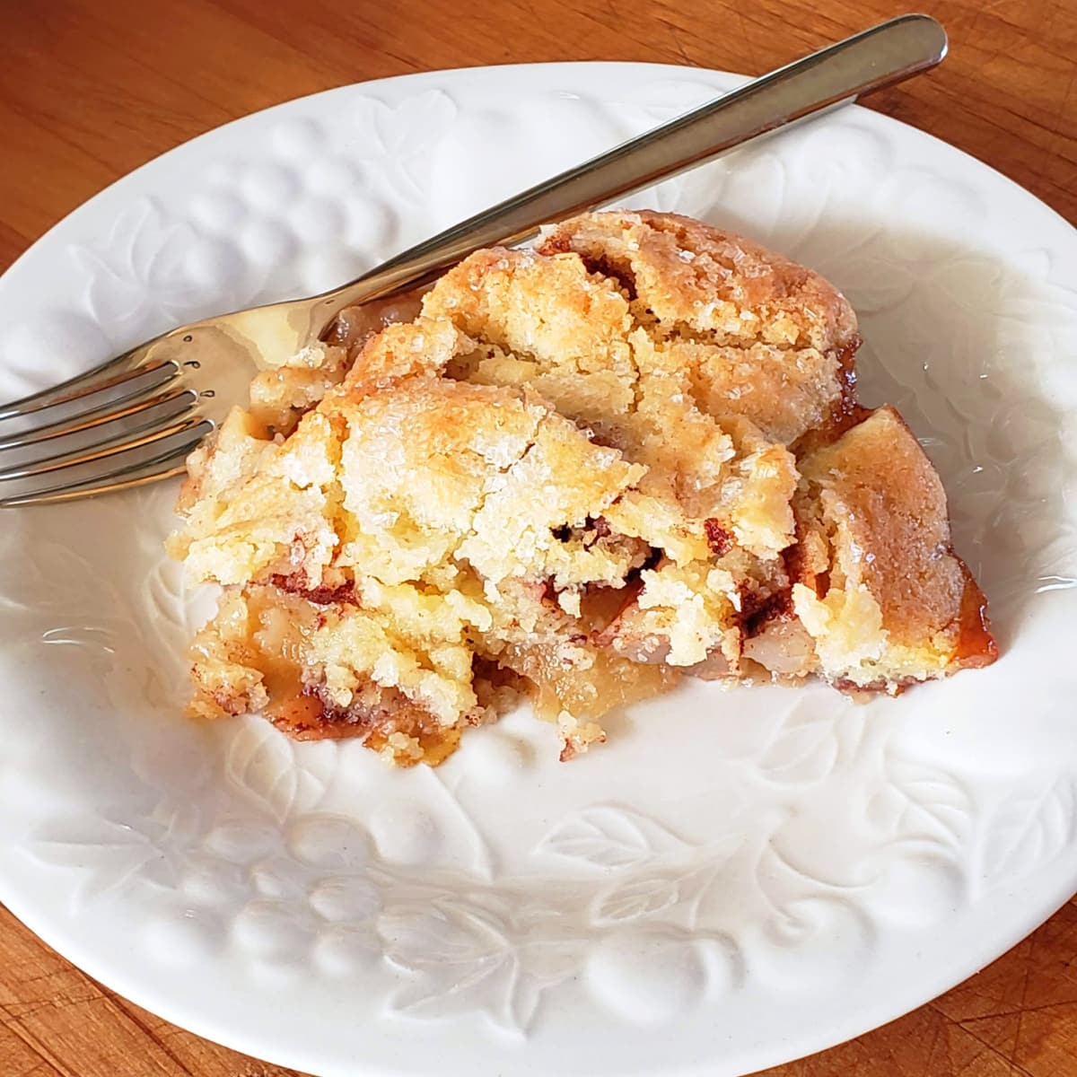 Sparkling sugar topping on Swedish Apple Pie slice on a white plate with fork alongside