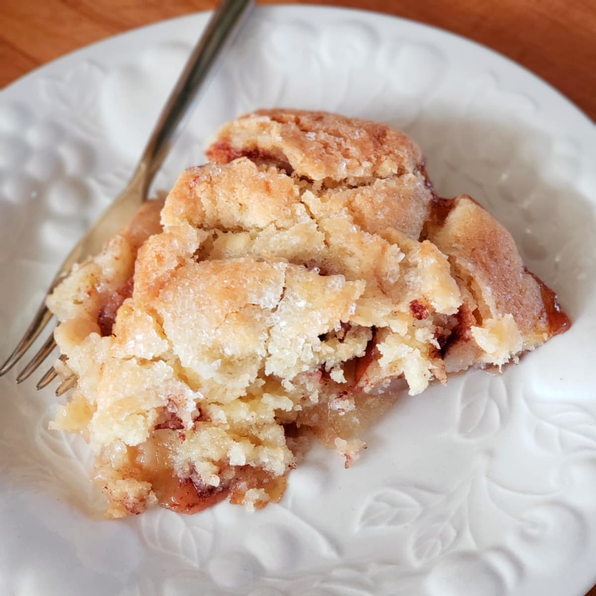 Slice of Swedish Apple Pie on a textured white plate with a fork alongside