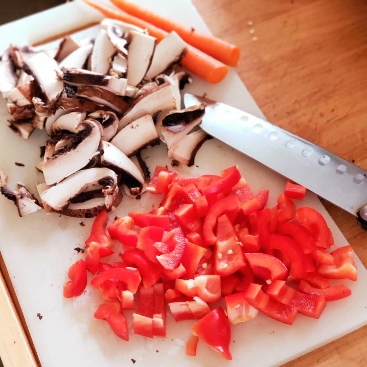Chop mushrooms and red pepper on a white cutting board