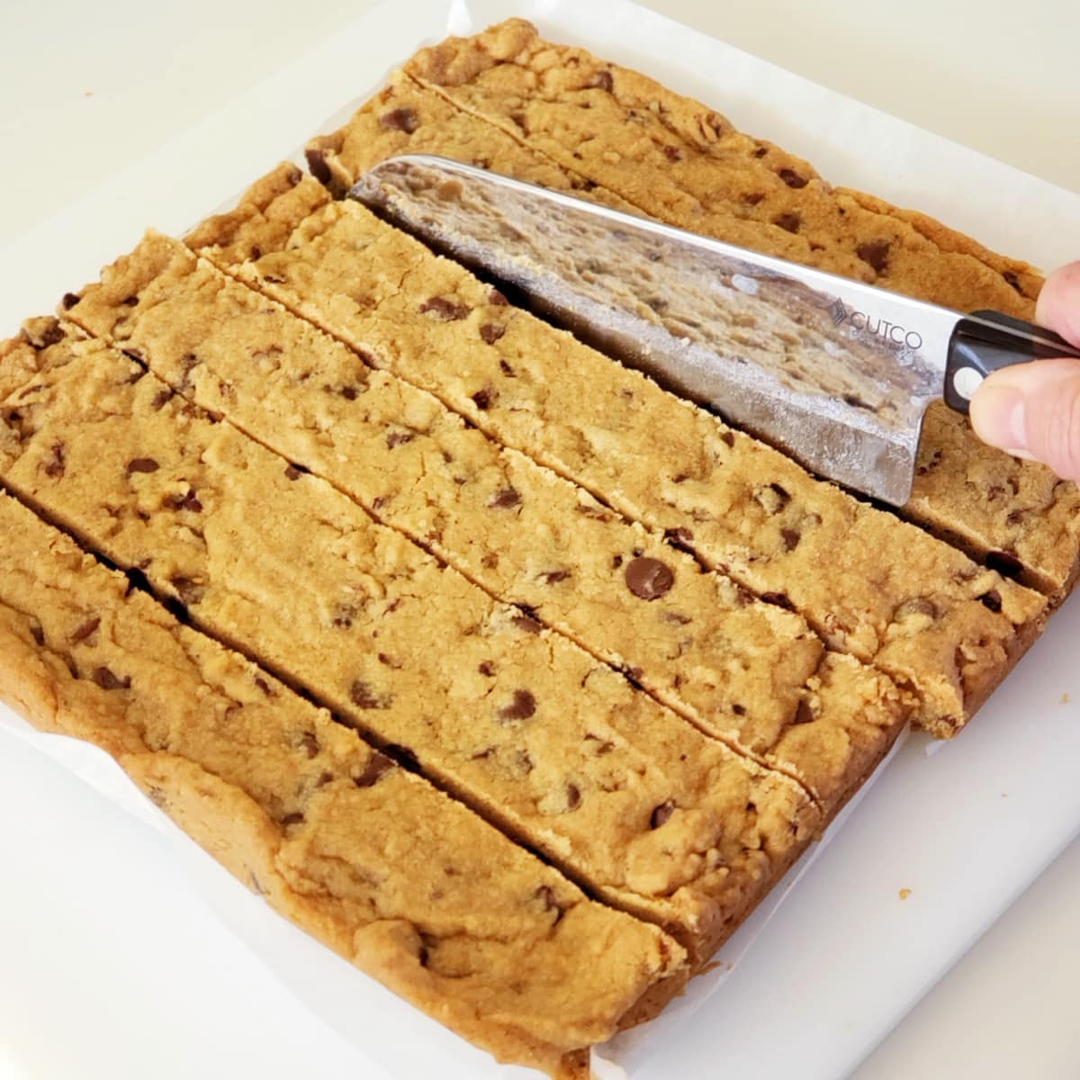 Hand holding a large knife cuts cookies into long strips