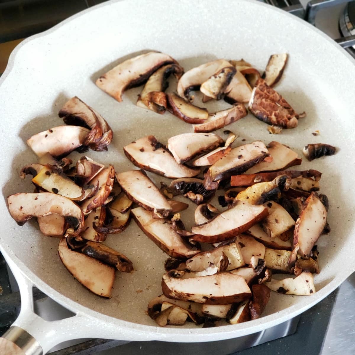 Sliced mushrooms frying in a light-colored skillet
