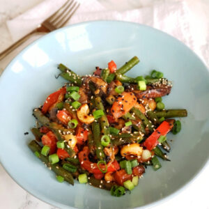 Variety of colorful cooked vegetables in a light blue bowl on a white counter top with a fork to the left