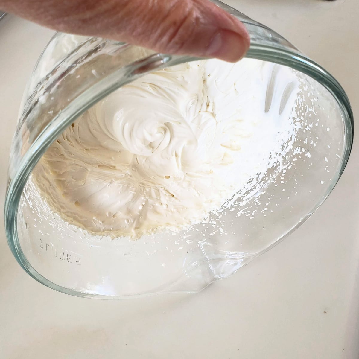 Mixing bowl with whipped cream being turned upside down to show how thick it is